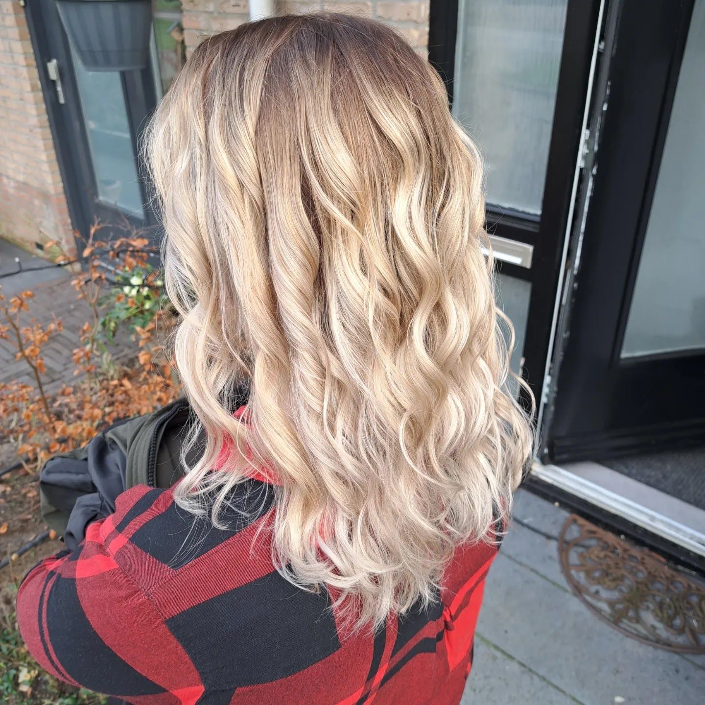 Blonde balayage met losse krullen, van achteren gezien bij de voordeur